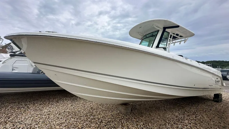 The Image of 2025 Boston Whaler 280 Outrage boat on gravel, under cloudy sky. - 0
