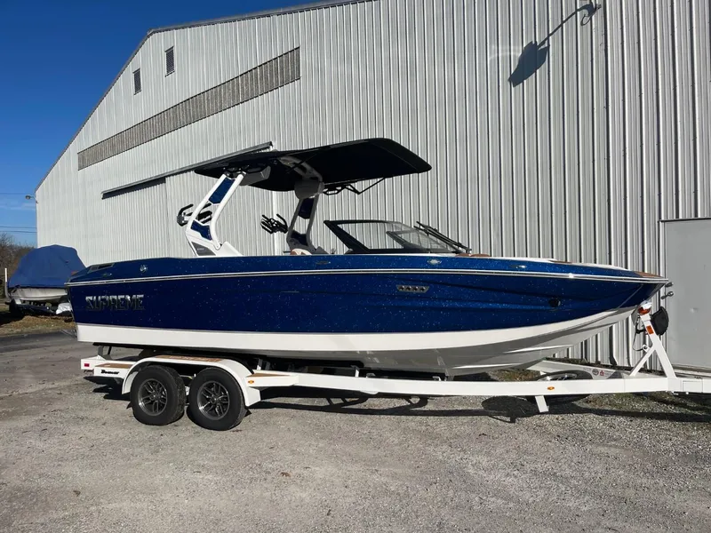 Slide: The Image of 2024 Supreme S220 boat on trailer, blue and white design, parked outdoors. - 12