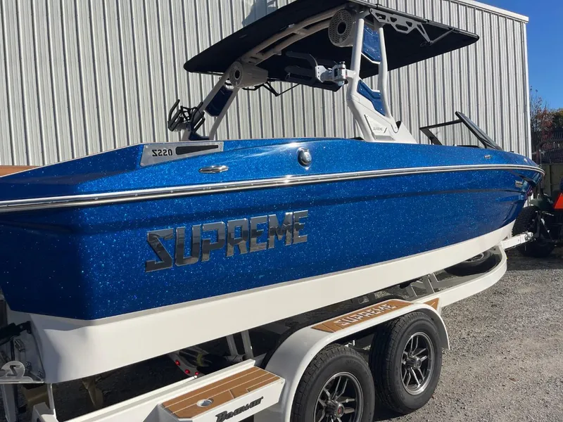 Slide: The Image of 2024 Supreme S220 boat in blue on a trailer, parked outdoors. - 14