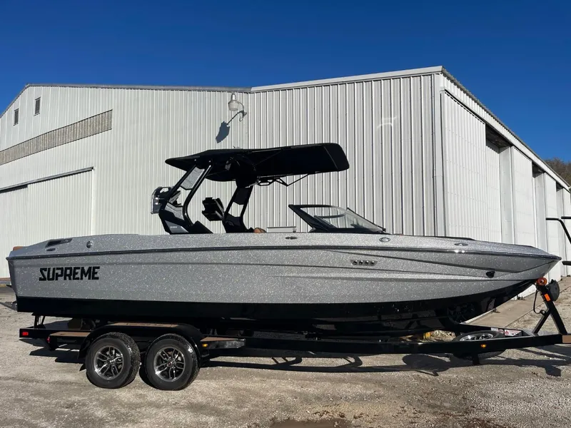 Slide: The Image of 2024 Supreme S240 boat on trailer, parked outside a warehouse. - 13