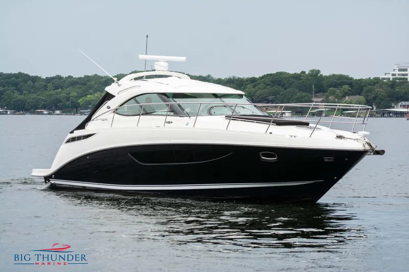 Slide: The Image of 2012 Sea Ray 410 Sundancer yacht on calm water, with lush green shoreline. - 2