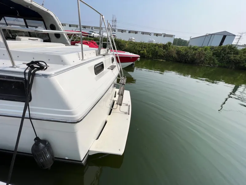 Slide: The Image of 1987 Carver Riviera 2807 boat docked on calm water, with nearby greenery and buildings. - 20