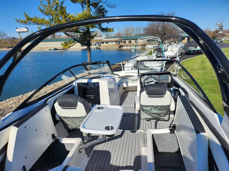 Slide: The Image of 2016 Yamaha Boats 242 Limited S interior with seating and table, docked by a lake. - 10