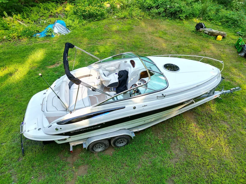 Slide: The Image of 2015 Crownline 236 boat on trailer, parked on grass, surrounded by greenery. - 0