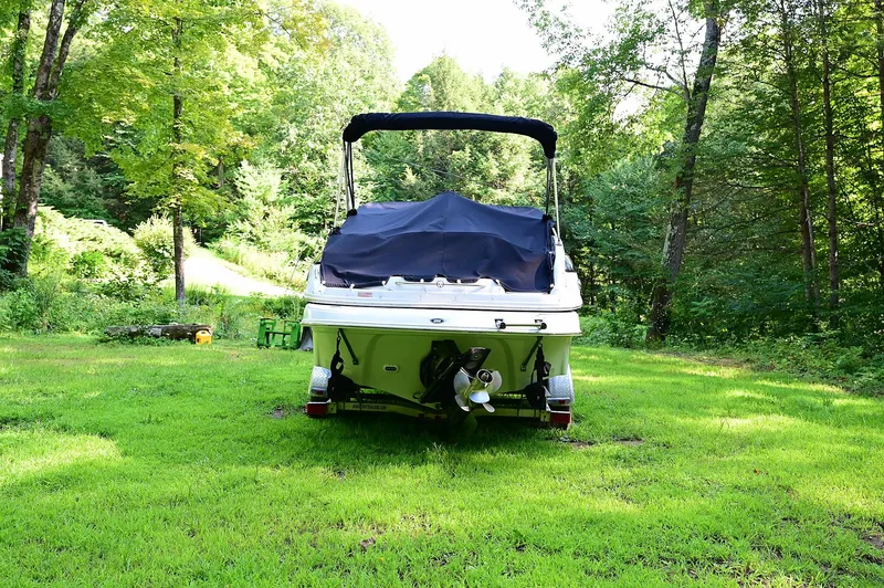 Slide: The Image of 2015 Crownline 236 boat parked on lush green grass, surrounded by trees. - 10