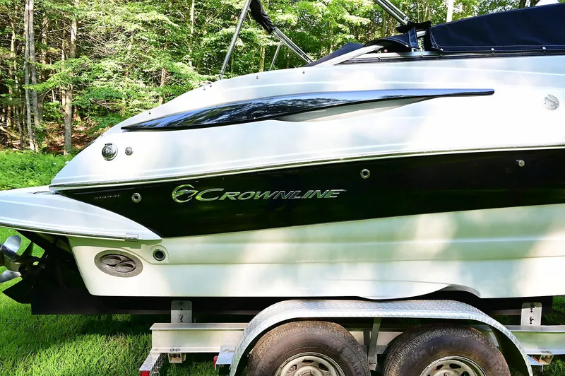 Slide: The Image of 2015 Crownline 236 boat on trailer, side view, in a wooded area. - 11