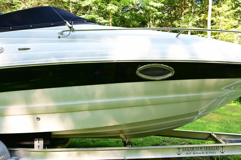 Slide: The Image of 2015 Crownline 236 boat on trailer, side view, in a lush green setting. - 12
