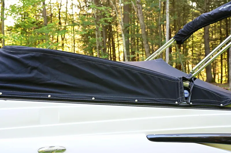 Slide: The Image of 2015 Crownline 236 boat with black cover in a wooded area. - 13