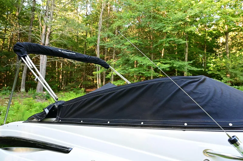 Slide: The Image of 2015 Crownline 236 boat with black cover, surrounded by lush green forest. - 14