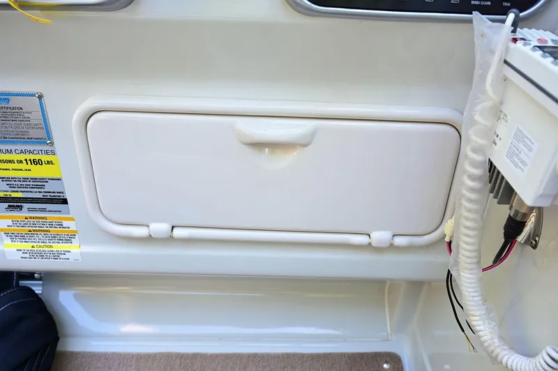 Slide: The Image of 2015 Crownline 236 boat interior storage compartment with control panel and safety labels. - 49