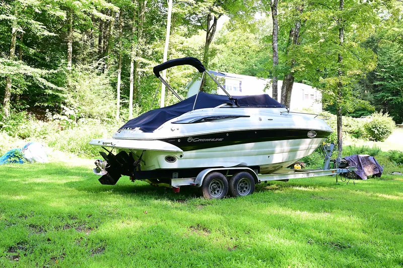 Slide: The Image of 2015 Crownline 236 boat on trailer, parked on lush green grass, surrounded by trees. - 5