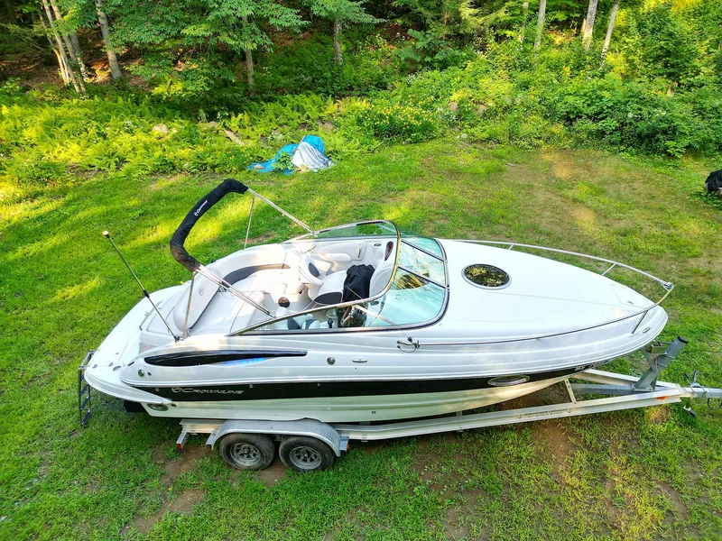 Slide: The Image of 2015 Crownline 236 boat on trailer, parked on grassy area with forest background. - 6