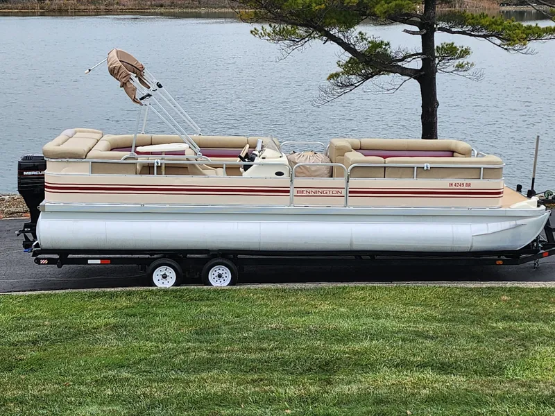 Slide: The Image of 2000 Bennington 2580LX pontoon boat on trailer by a lake. - 0
