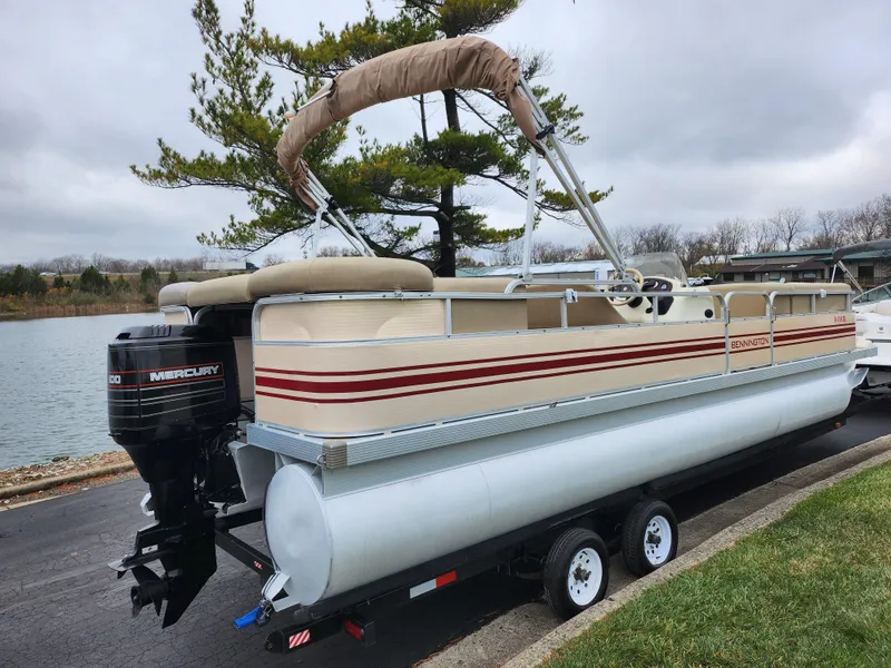Slide: The Image of 2000 Bennington 2580LX pontoon boat on trailer by a lake. - 1