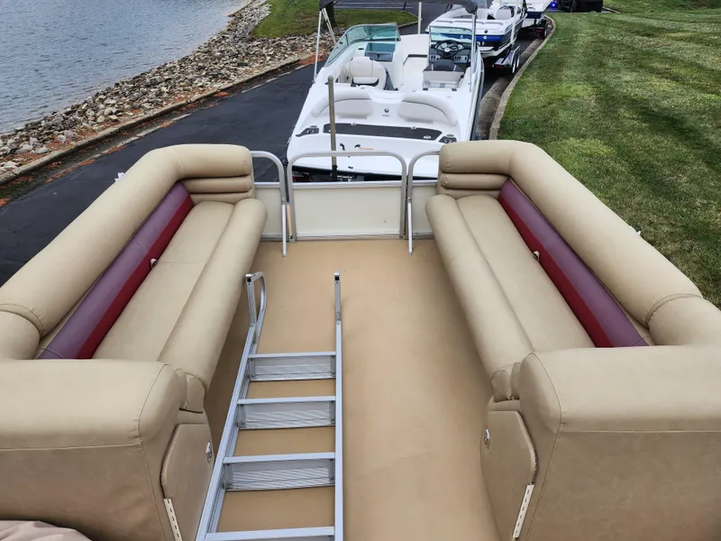 Slide: The Image of Bennington 2580LX 2000 pontoon boat with beige seating and ladder, docked by the lake. - 23
