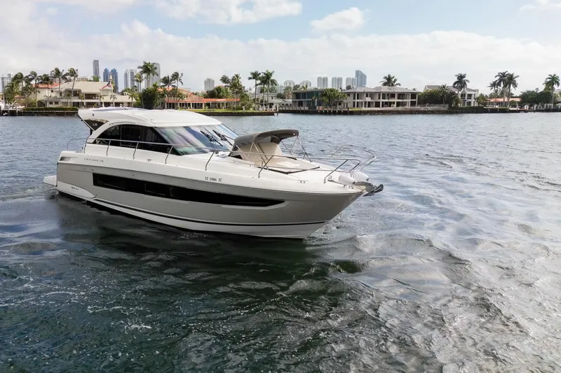 The Image of 2018 Jeanneau Leader 46 yacht cruising on a sunny waterfront with palm trees. - 1