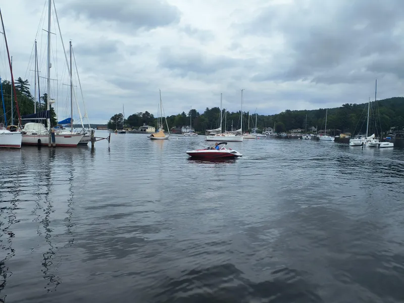 Slide: The Image of 2025 Scarab 165 LX boat cruising in a marina with sailboats and cloudy sky. - 2