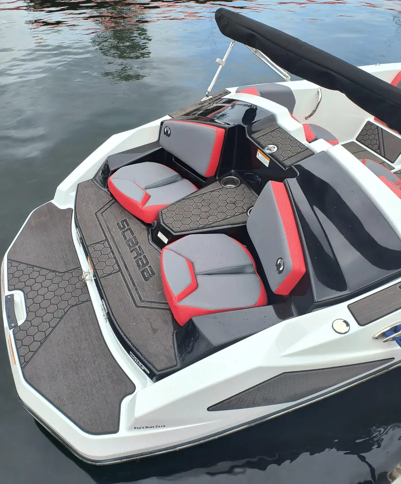 Slide: The Image of 2025 Scarab 165 LX boat with red and gray seating, docked on calm water. - 6