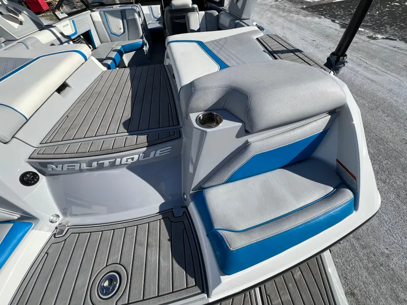 Slide: The Image of 2020 Nautique G21 boat interior with gray and blue seating, cup holder, and branded flooring. - 14