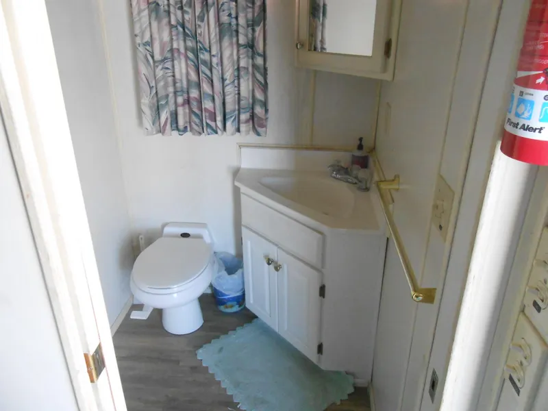 Slide: The Image of Compact bathroom in 1998 Lakeview 5516 model with toilet, sink, and floral curtains. - 10