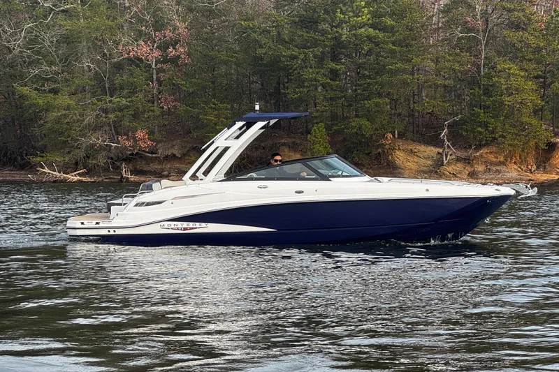 Slide: The Image of 2025 Monterey M6 boat cruising on a serene lake with forested shoreline. - 2