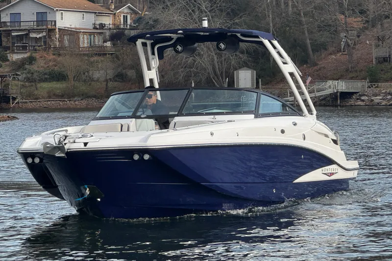 Slide: The Image of 2025 Monterey M6 boat cruising on a lake near rustic houses and trees. - 5