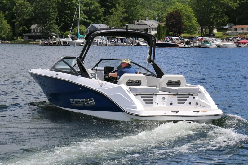Slide: The Image of 2025 Scarab 235 SE boat cruising on a scenic lake with lush greenery. - 2
