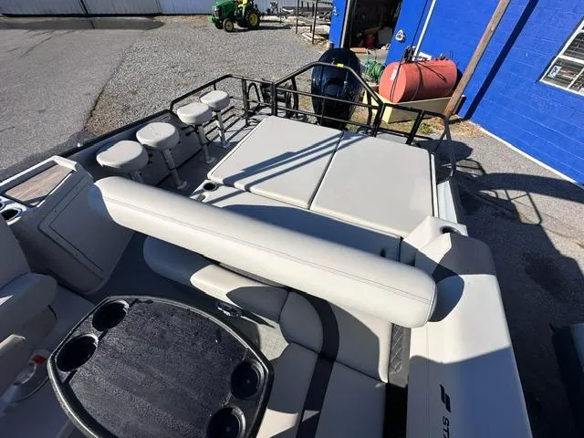 Slide: The Image of 2025 Starcraft CX 23 DL BAR boat interior with seating and table, parked near a blue building. - 6