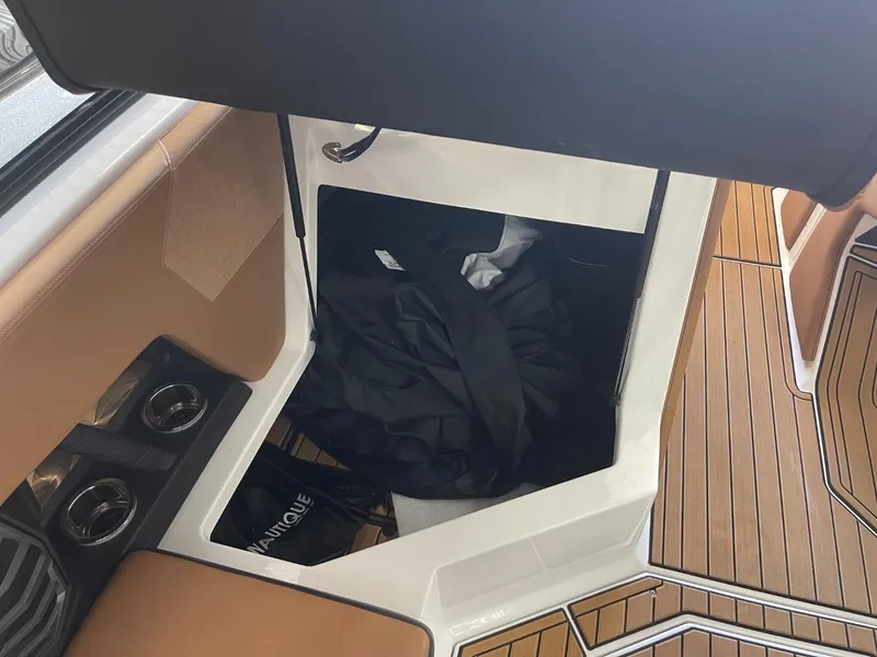 Slide: The Image of 2024 Nautique Super Air Nautique G23 storage compartment with teak flooring and cup holders. - 18