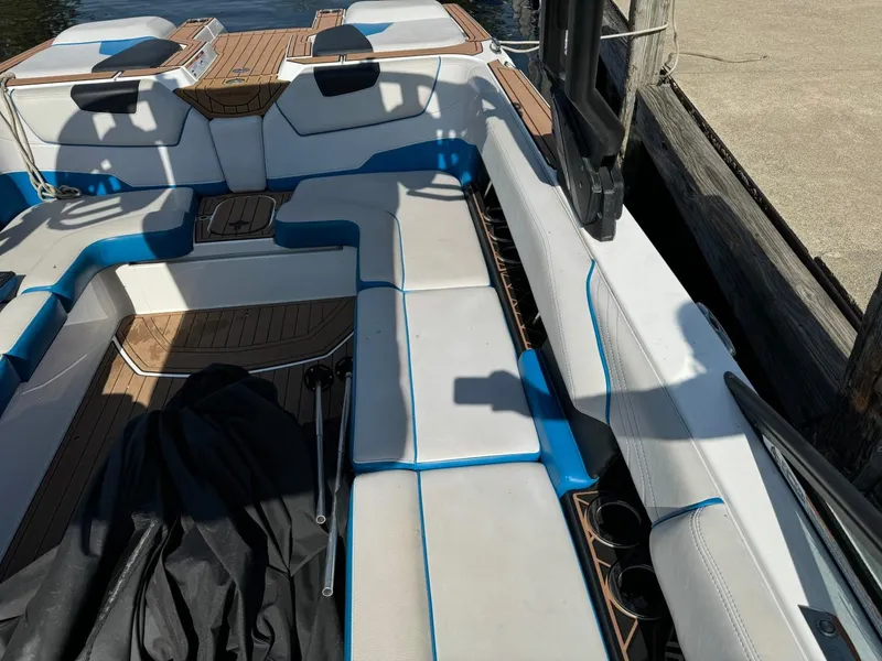 Slide: The Image of 2018 Nautique Super Air Nautique GS24 interior with white and blue seating, docked by the water. - 12