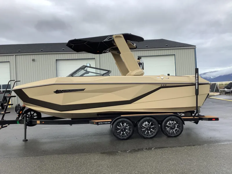 Slide: The Image of 2025 Nautique G23 boat on trailer, beige color, parked outside industrial building. - 1