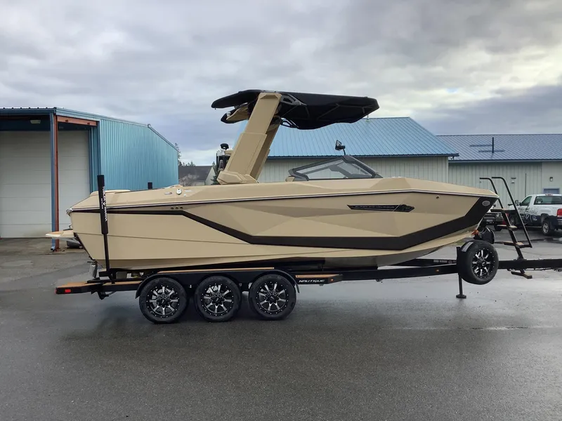 Slide: The Image of 2025 Nautique G23 boat on trailer, parked outdoors near blue buildings. - 5