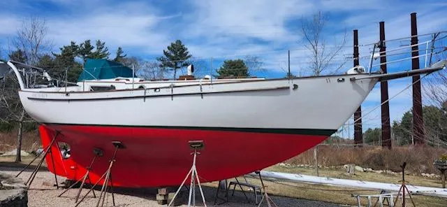 The Image of 1980 Kaiser Gale Force 34 sailboat on stands, red hull, outdoors under blue sky. - 0