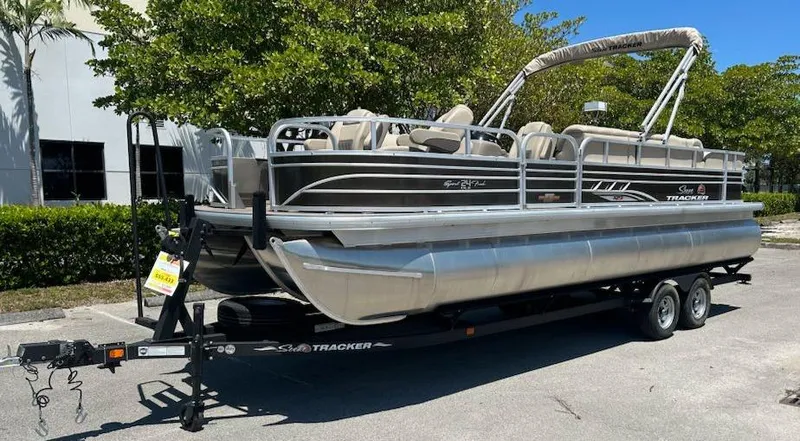 Slide: The Image of 2025 Sun Tracker Sportfish 24 XP3 pontoon boat on trailer, parked outdoors. - 2