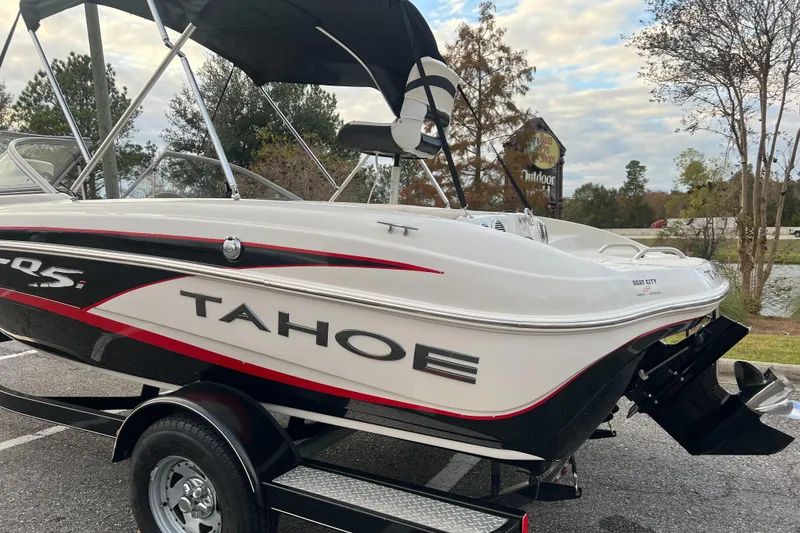 Slide: The Image of 2013 Tahoe Q5i boat on trailer, parked outdoors near trees and water. - 2