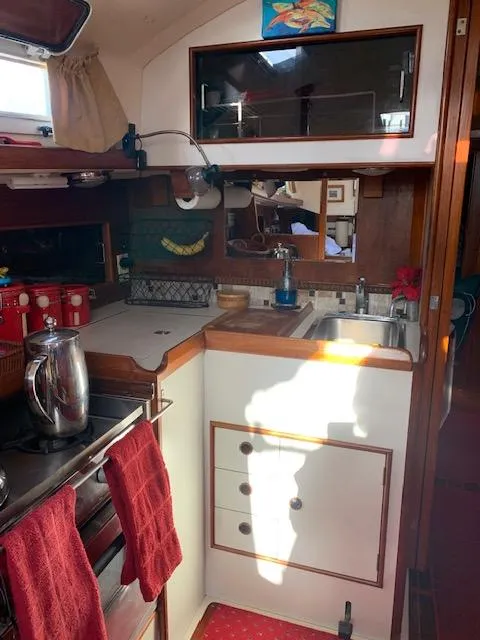 Slide: The Image of 1986 Nonsuch 30 Ultra yacht interior kitchen with wooden cabinets and red accents. - 38
