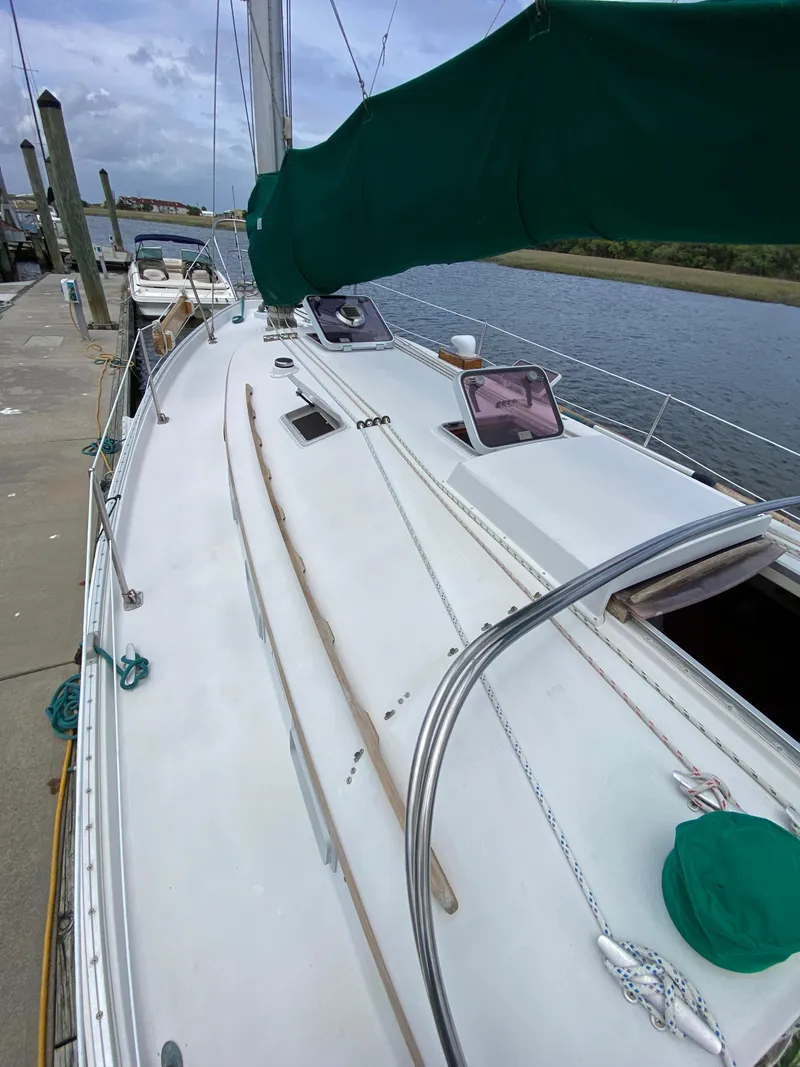 Slide: The Image of 1986 Nonsuch 30 Ultra sailboat docked by a river, featuring green sail cover. - 7