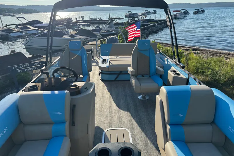 Slide: The Image of 2025 Bennington 23 SSB pontoon boat with blue and beige seating, docked by a lake. - 21