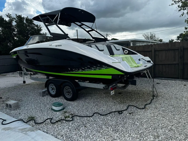 Slide: The Image of 2021 Yamaha AR250 boat on trailer, black and green design, parked on gravel. - 2