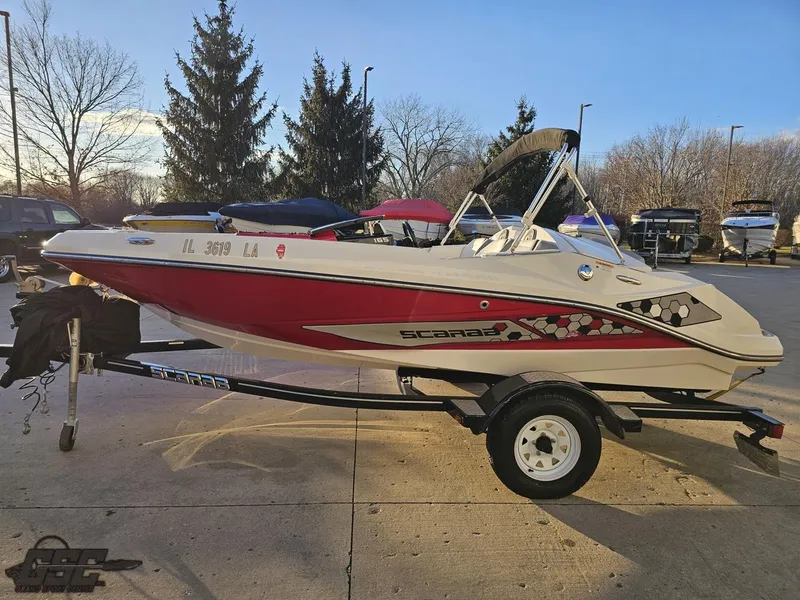 Slide: The Image of 2018 Scarab 165 ID boat on trailer, parked outdoors, with trees in the background. - 19