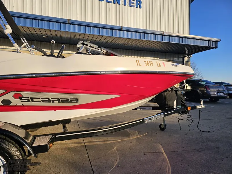 Slide: The Image of 2018 Scarab 165 ID boat on trailer, red and white design, parked outside a building. - 3