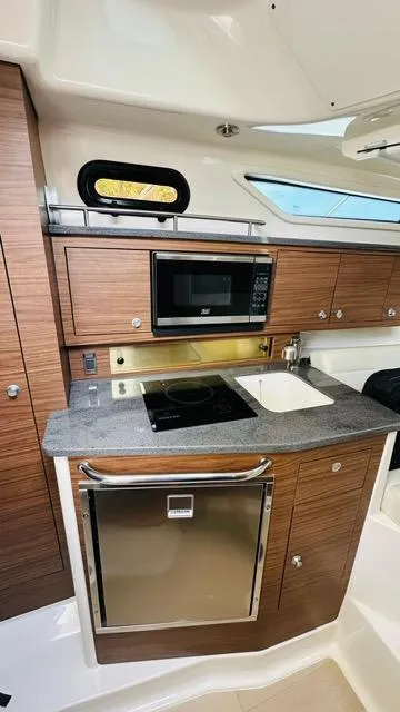 Slide: The Image of 2023 Boston Whaler 325 boat kitchen with wood cabinets, microwave, sink, and stove. - 16
