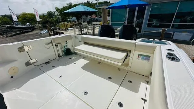 Slide: The Image of 2023 Boston Whaler 325 boat deck with seating, docked near umbrellas and a building. - 6