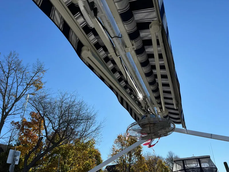 Slide: The Image of Custom MKI Pontoon Boat 2022 with striped canopy, under clear blue sky. - 4
