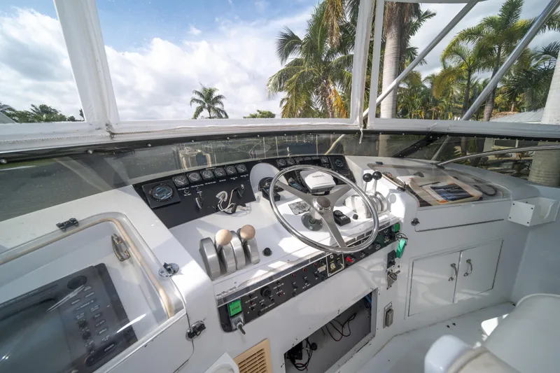Slide: The Image of 1999 Hatteras 52 Cockpit Motor Yacht helm with steering wheel and controls, surrounded by palm trees. - 14