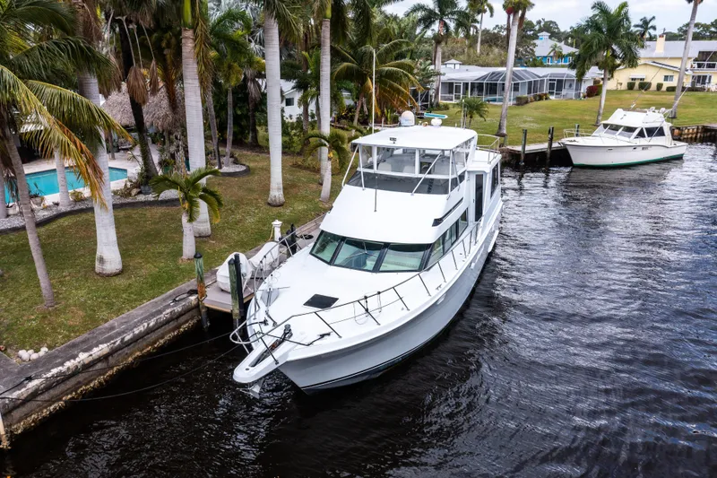 Slide: The Image of 1999 Hatteras 52 Cockpit Motor Yacht docked by palm trees in a serene canal. - 4