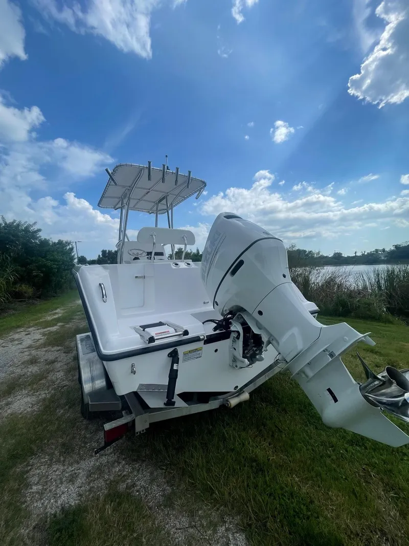 Slide: The Image of 2024 Aquasport 220 CC boat with outboard motor, parked near a lake under a blue sky. - 11