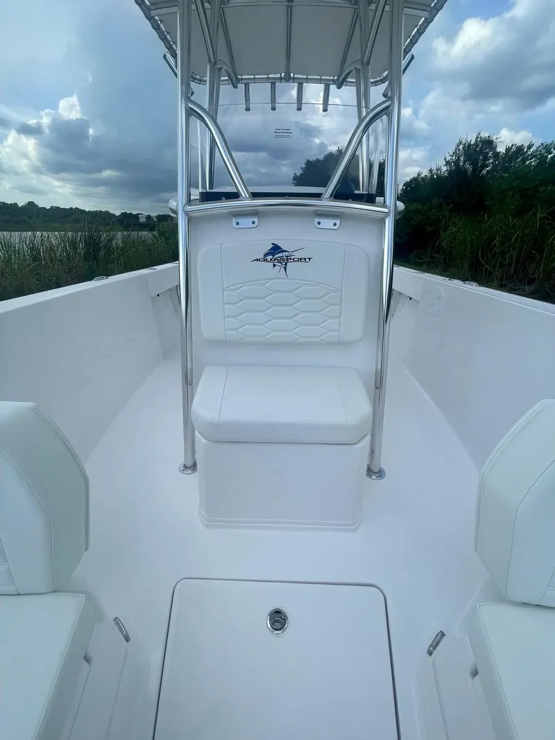 Slide: The Image of 2024 Aquasport 220 CC boat interior with seating and console, under cloudy sky. - 5