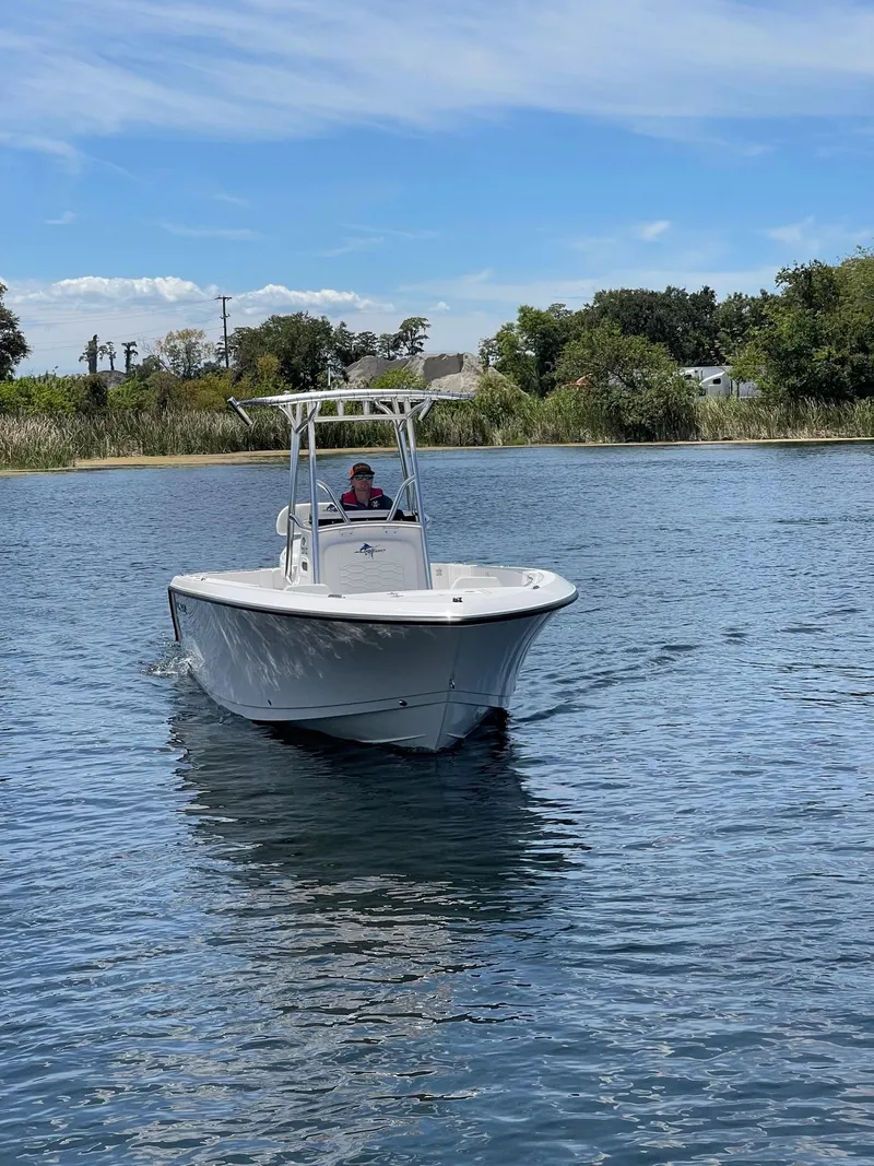 Slide: The Image of 2024 Aquasport 220 CC boat cruising on a calm lake under a clear blue sky. - 6