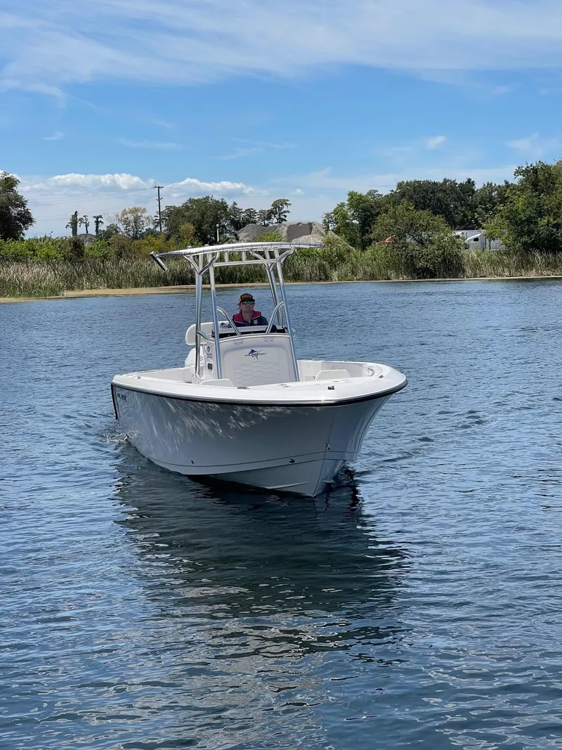 Slide: The Image of 2024 Aquasport 220 CC boat cruising on a calm lake under a clear sky. - 7